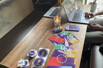 Campaign materials, including flyers reading "Volt, We unite Europe" and stickers with portraits, arranged on a long cafe table near open laptops.
