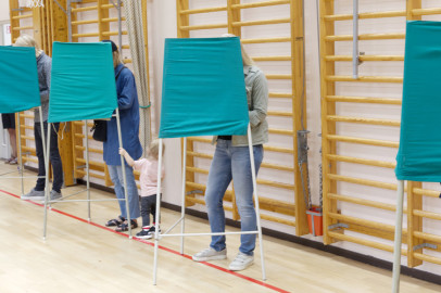 Voters standing inside green fabric voting booths lined up in a gymnasium.