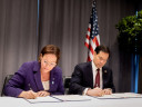 Maria Malmer Stenergard and Marco Rubio sitting at a table, signing official documents in front of an American flag.
