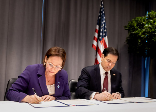 Maria Malmer Stenergard and Marco Rubio sitting at a table, signing official documents in front of an American flag.