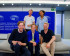 Five people posing on and behind a couch in front of a blue wall featuring the European Parliament logo.