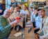 A group of seven people, some wearing white Volt t-shirts, smiling together at a long cafe table with drinks.